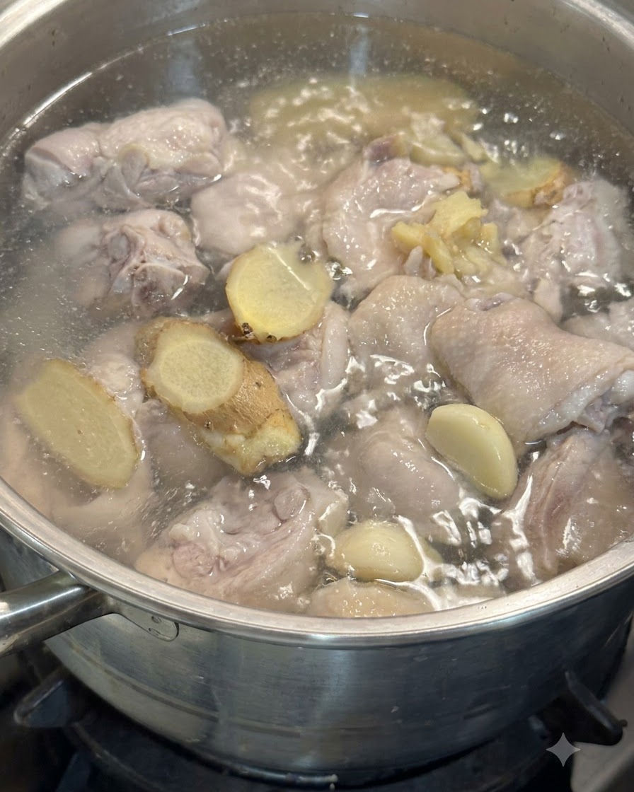 simmering water の中で、ニンニクの粒や生姜のスライスが鶏肉と一緒に浮いている様子。