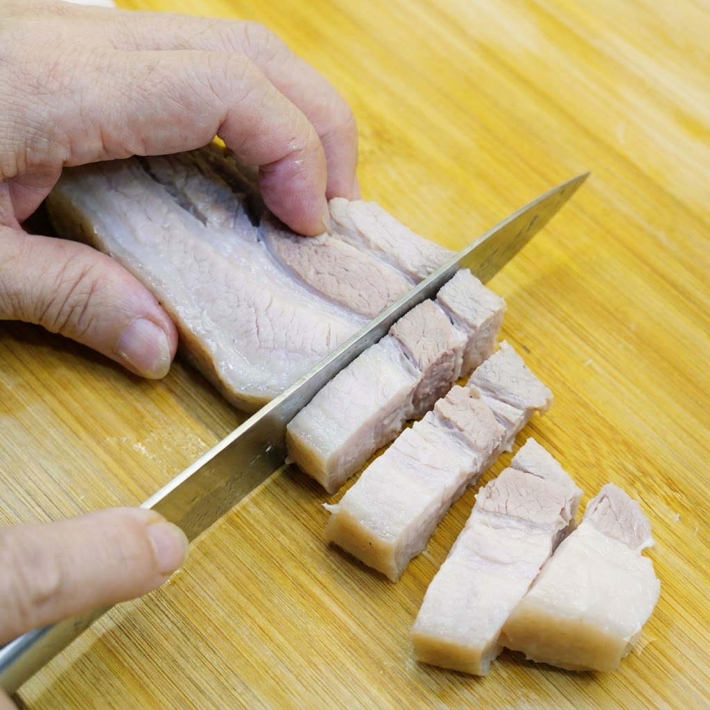茹でた豚バラ肉が木製のまな板の上で一口大にスライスされている様子。