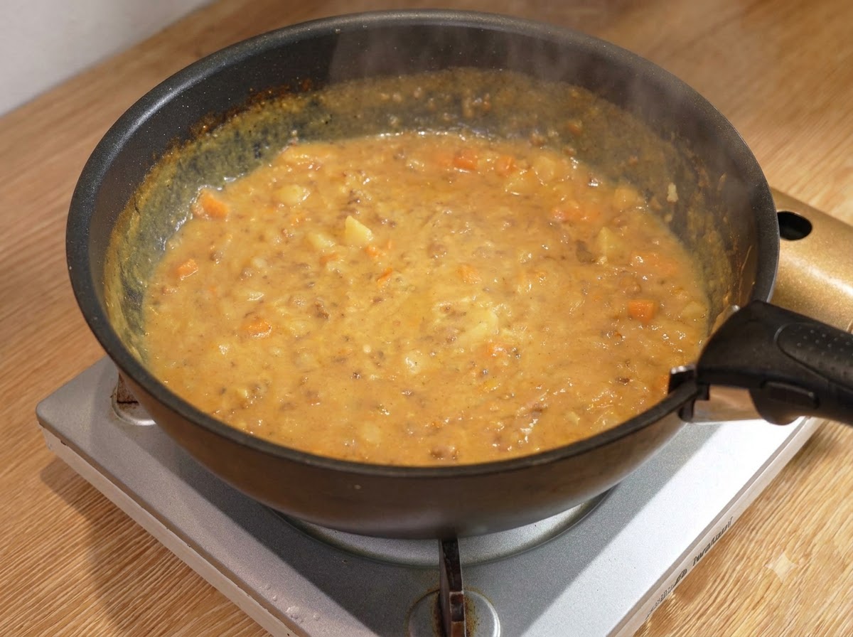 黒いフライパンの中で、木べらで混ぜられながらとろみが付いてきているカレーミートソース。