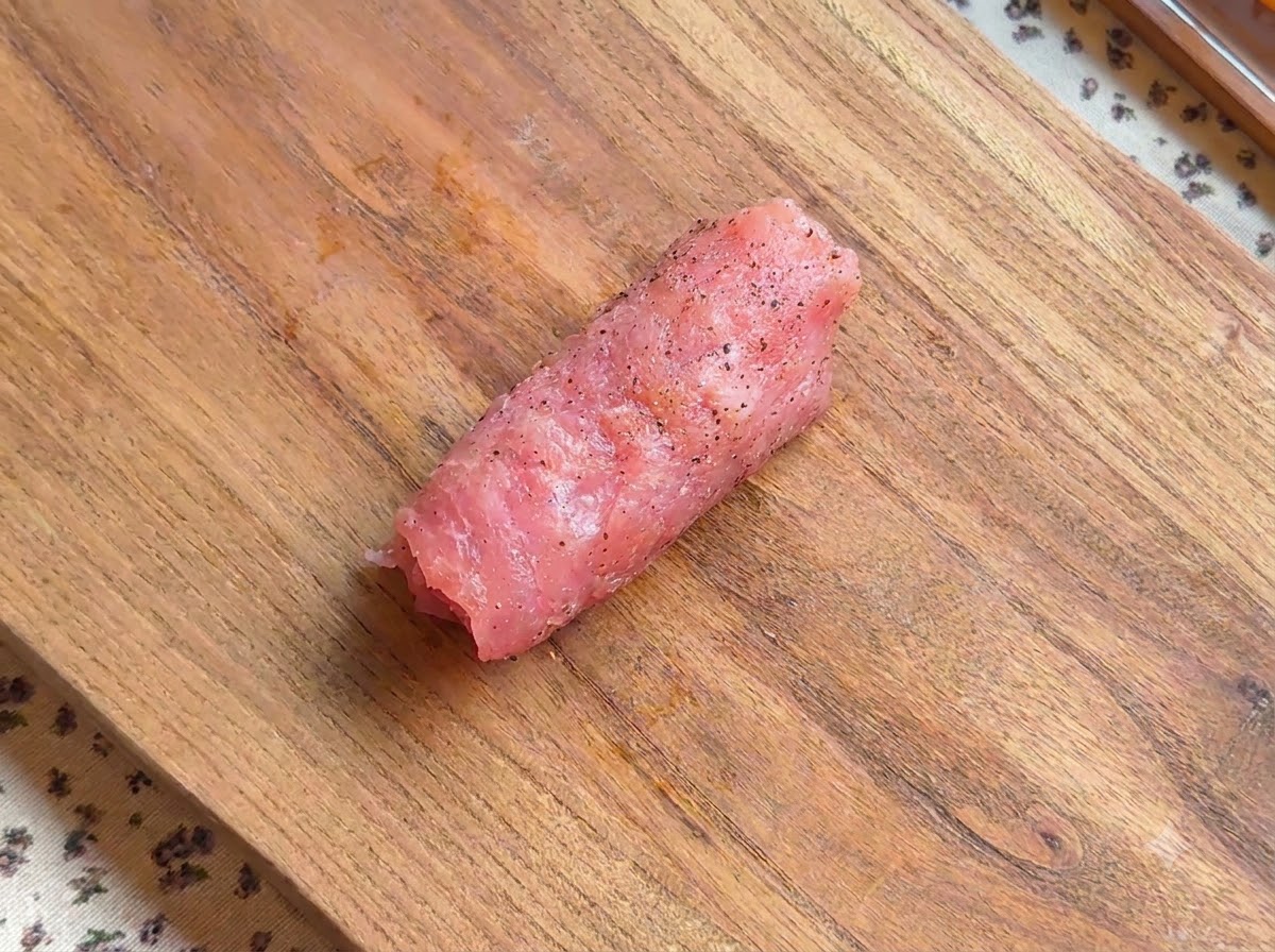 木製のボードの上に置かれた、成形された下味付きの豚肉カツレツロール。