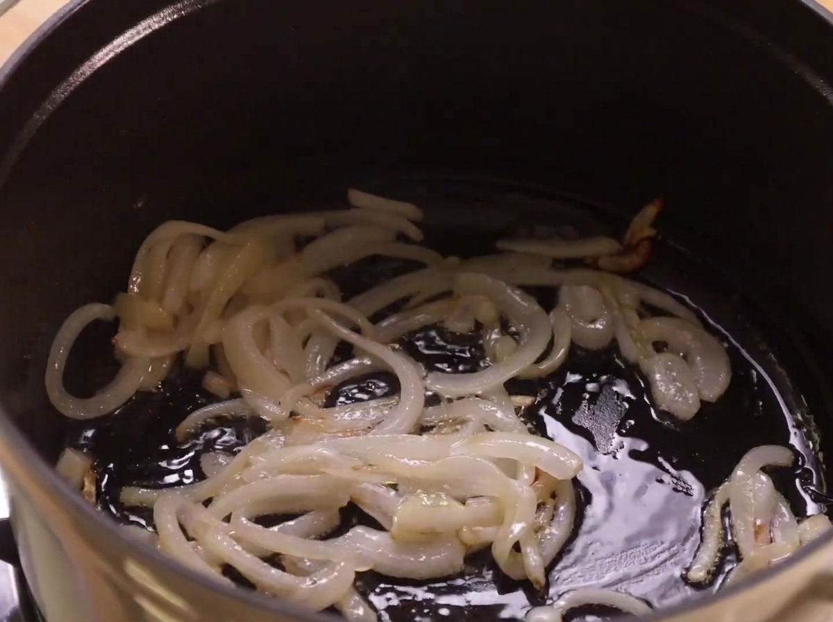 黒っぽい調理鍋の底で油の中でタマネギが炒められている様子。