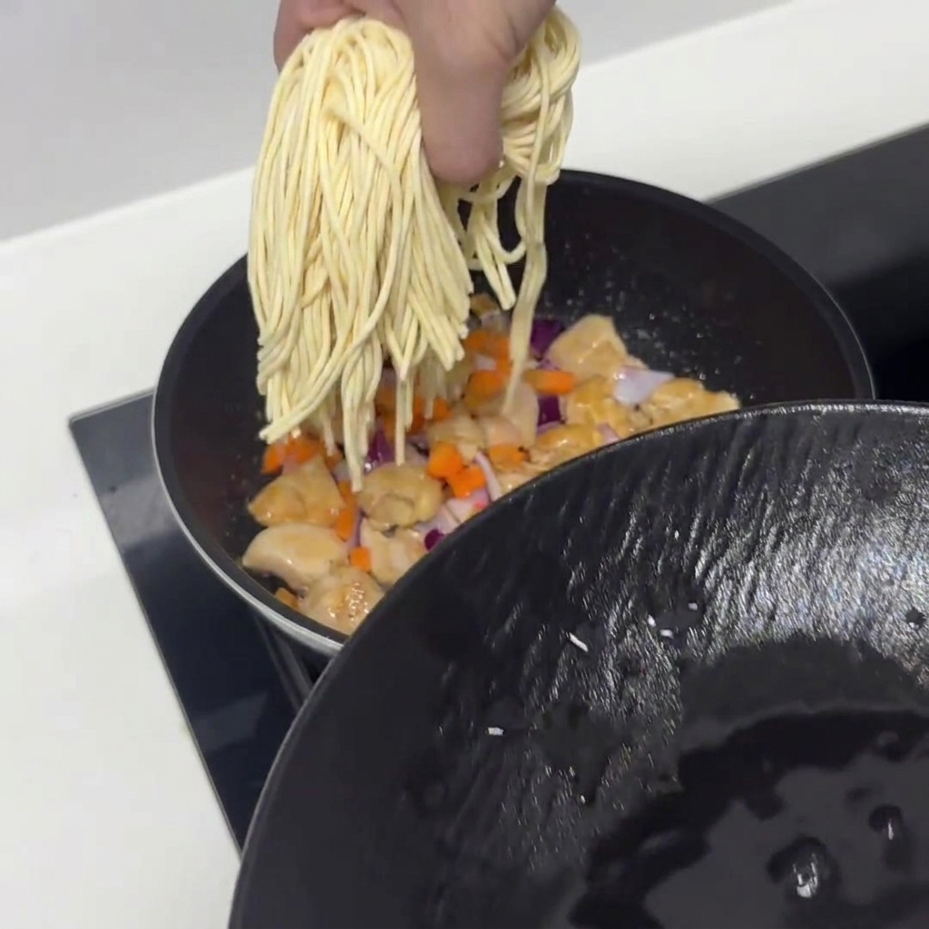 あらかじめ30分間水に浸したパスタ麺を、鶏肉と野菜の入ったフライパンに投入している様子。