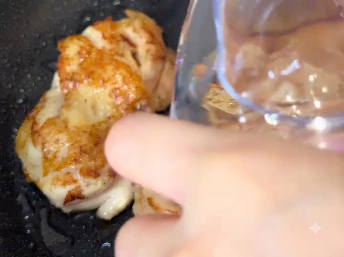 容器から鶏肉の入ったフライパンに直接水が注がれている様子。