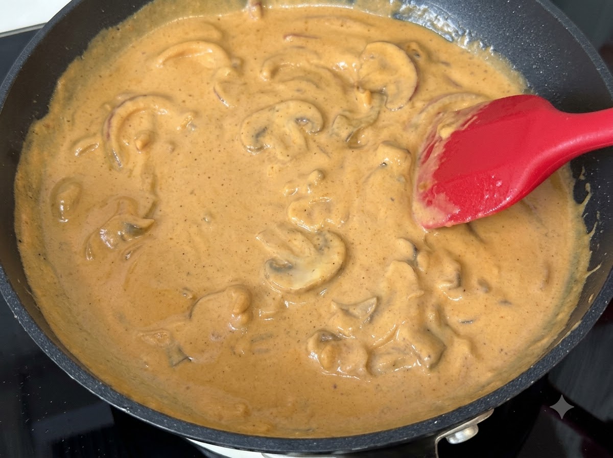 フライパンで煮込んでいるカレークリームソースに、スライスしたマッシュルームが混ぜ合わされている様子。