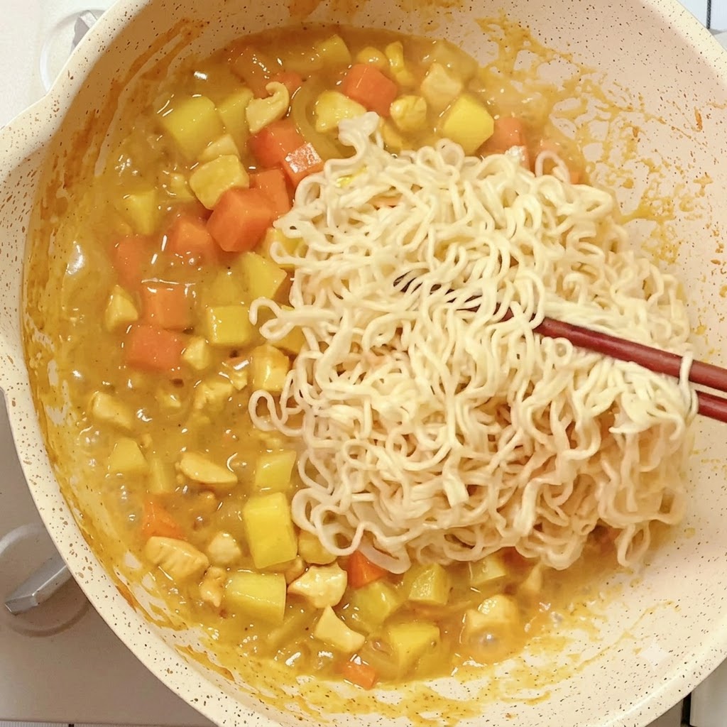 箸を使って、茹でておいたインスタントラーメンを煮詰まったカレーのフライパンに入れている様子。