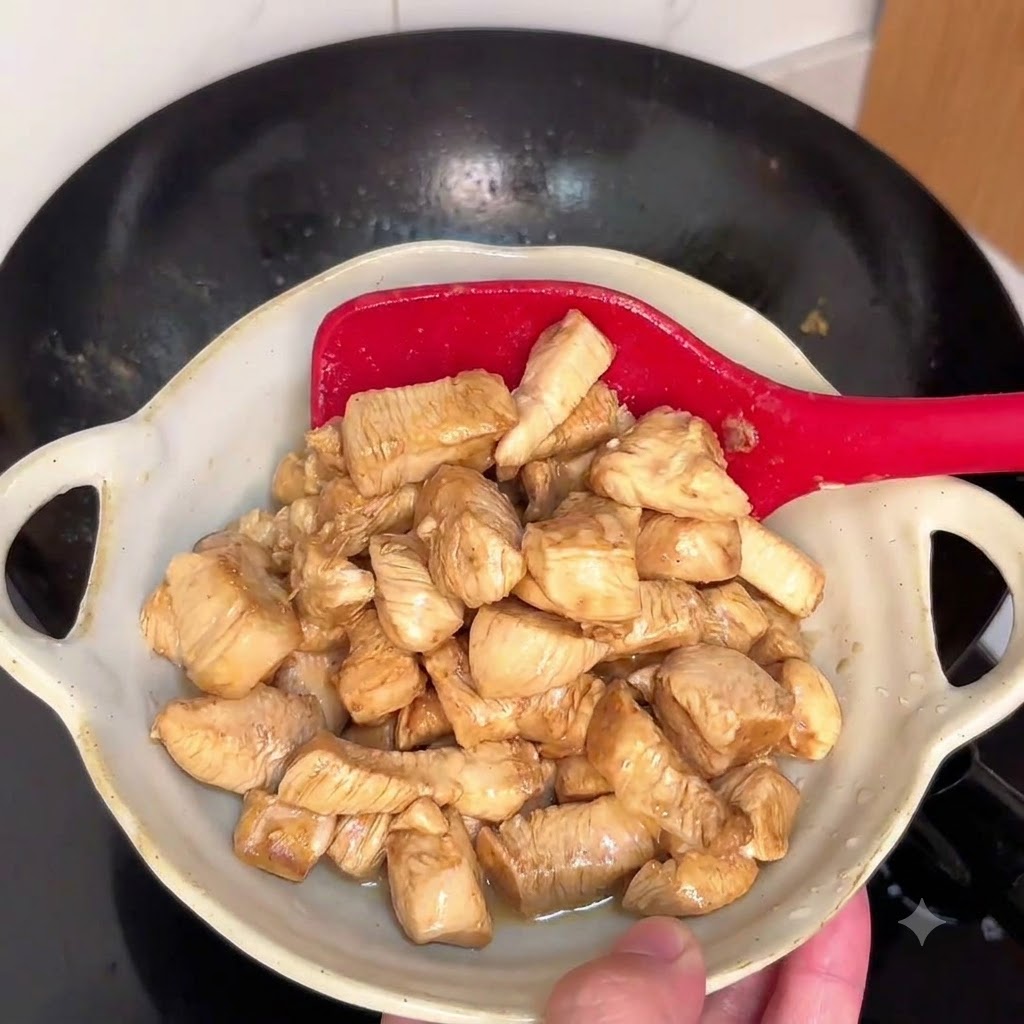 赤いヘラを使って熱した中華鍋で鶏肉を炒めている様子。