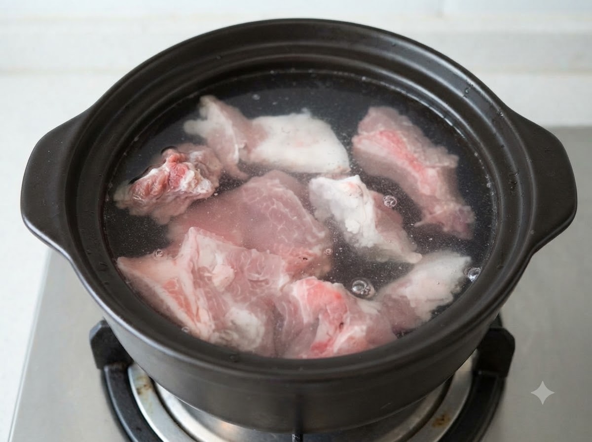 黒い土鍋の中で冷水に浸された生の豚骨のぶつ切り。