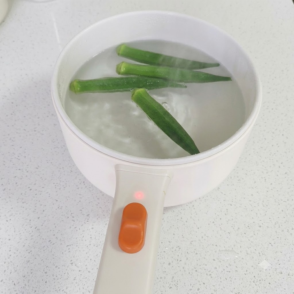 沸騰した鍋から箸で引き上げられる緑色の茹でオクラ