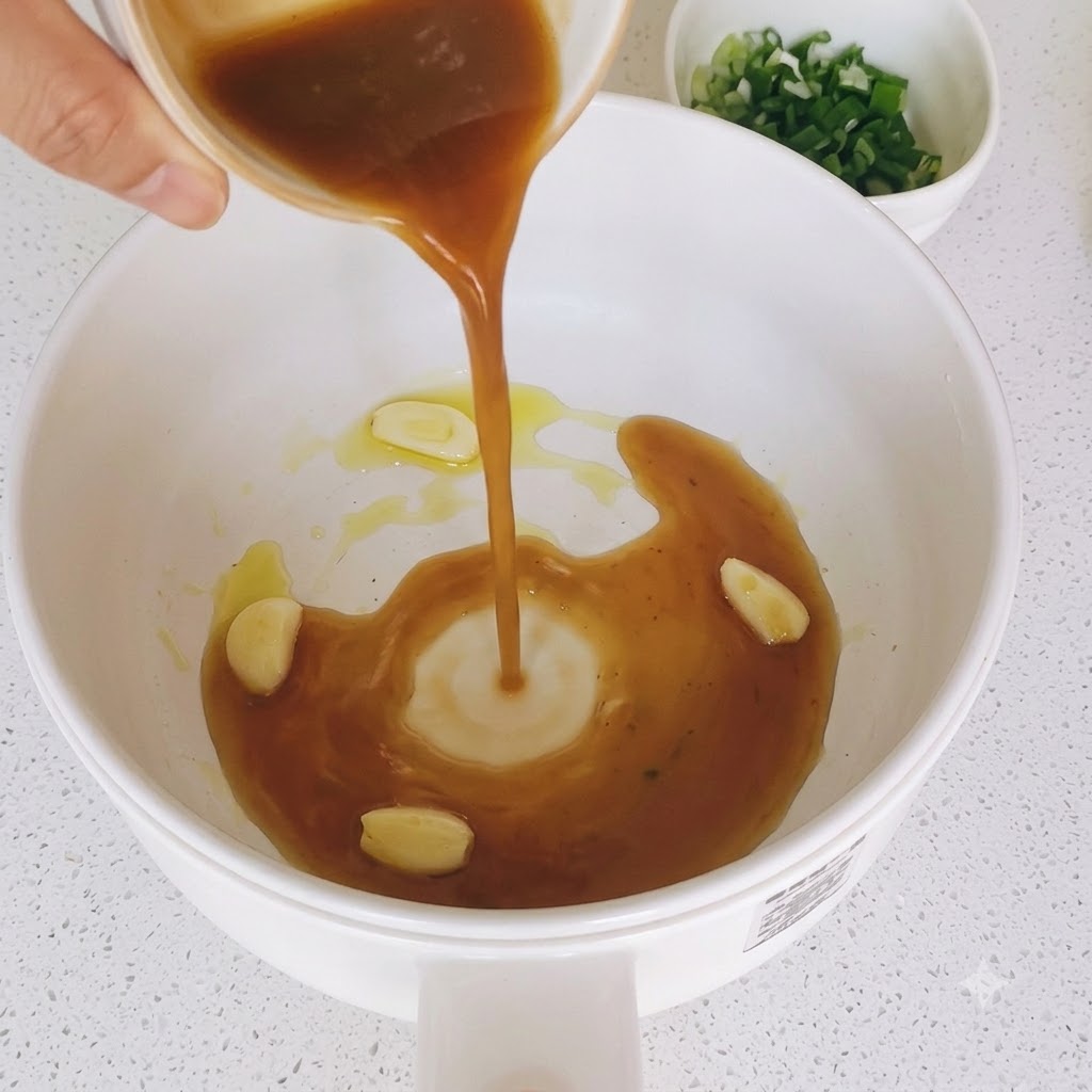 炒めたにんにくの入ったフライパンに茶色のタレが注がれている様子