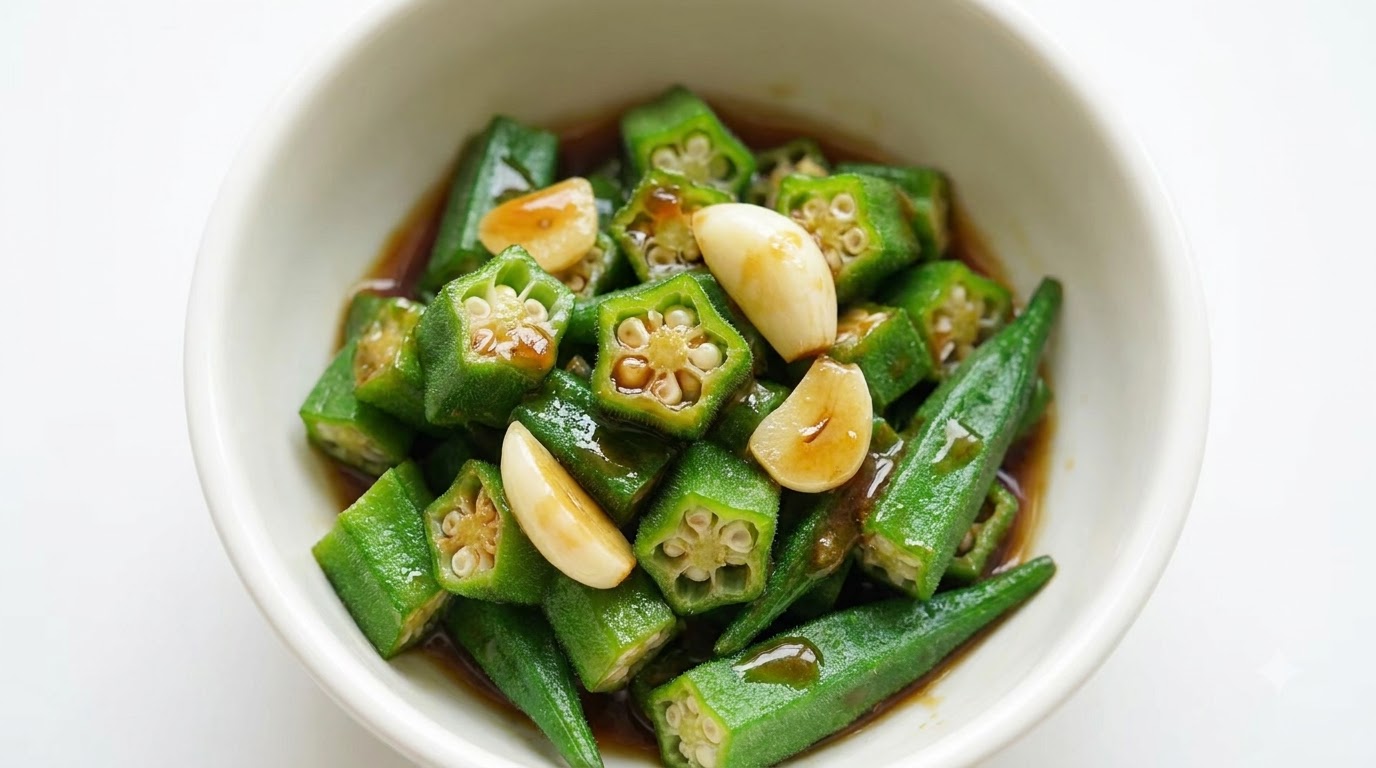 刻んだにんにくと濃厚な茶色のタレがかかった、緑色の茹でオクラの盛り付け
