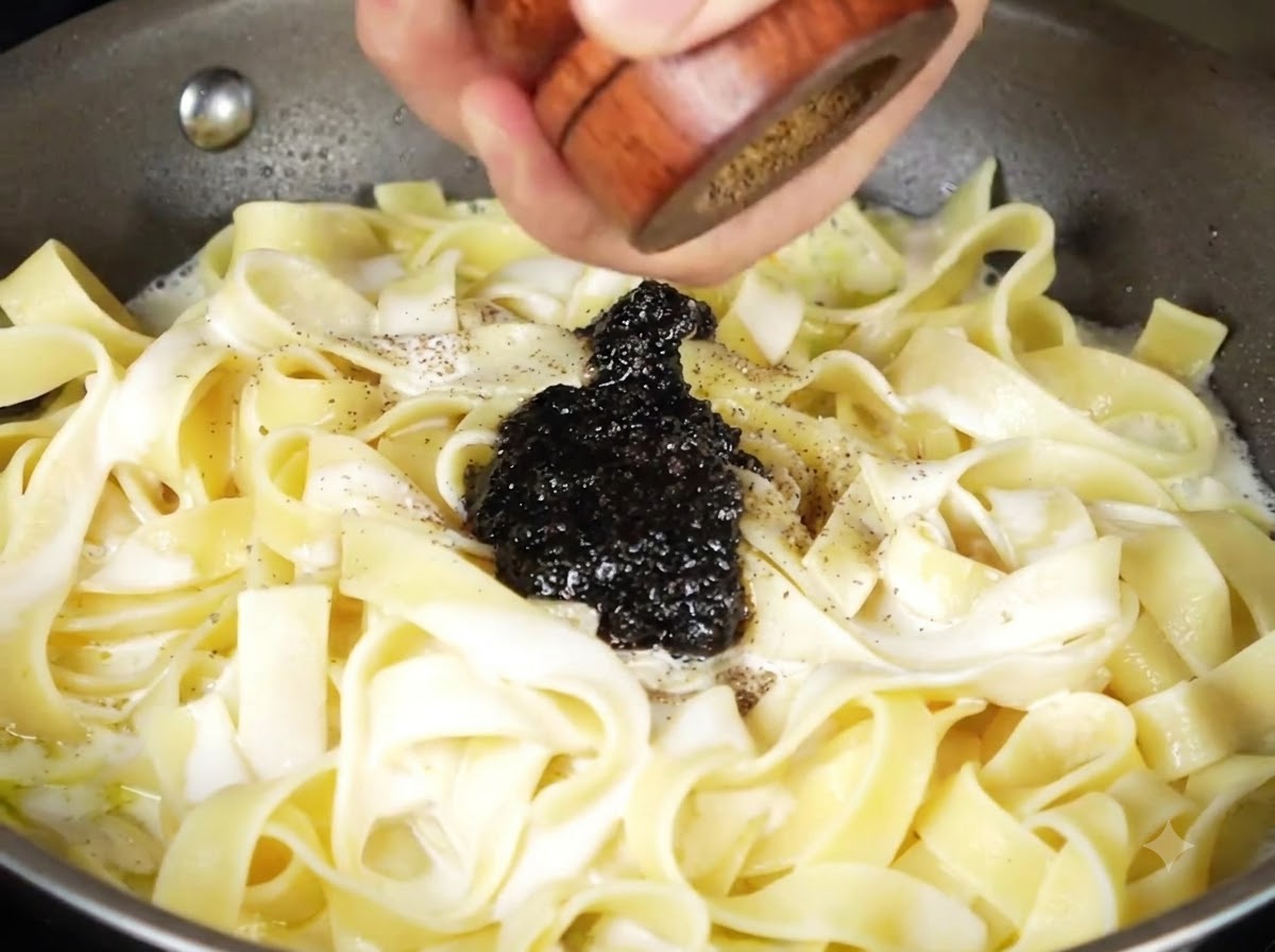 フライパンのクリーミーなパスタの上に、黒トリュフソースと挽きたての黒コショウが乗っている様子。