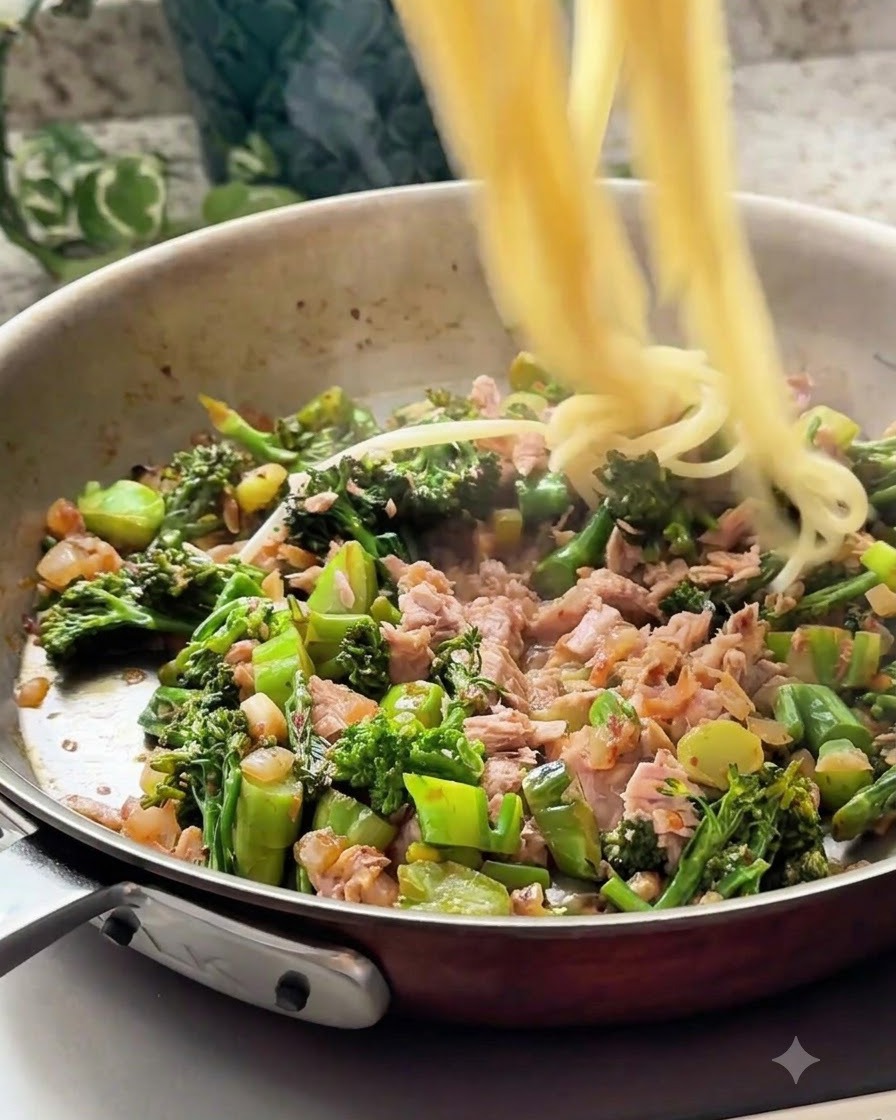 茹でたスパゲッティの麺が、ツナと野菜のミックスが入ったフライパンに投入されている様子。