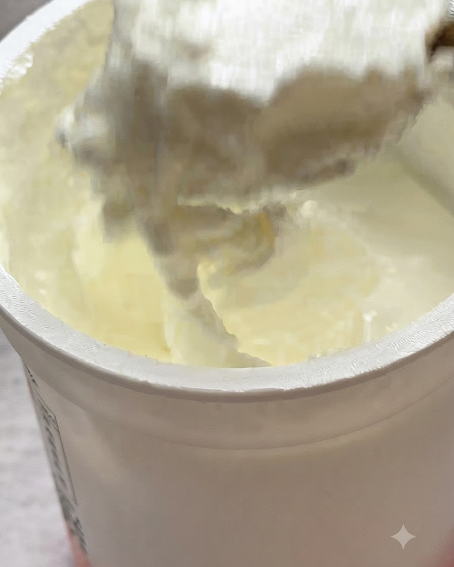 フライパンの中のパスタの上に、スプーン一杯の無糖ヨーグルトが加えられている様子。
