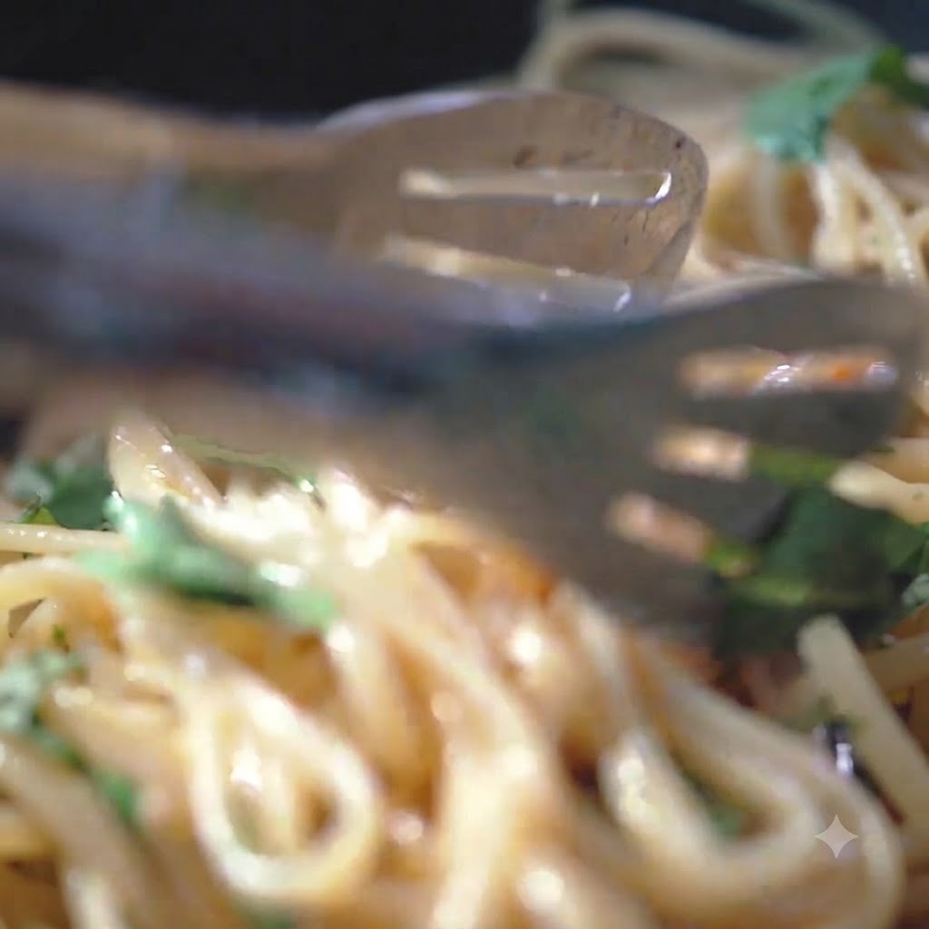熱々のフライパンの中にあるパスタの麺に、黒こしょうと海塩が振りかけられている様子。
