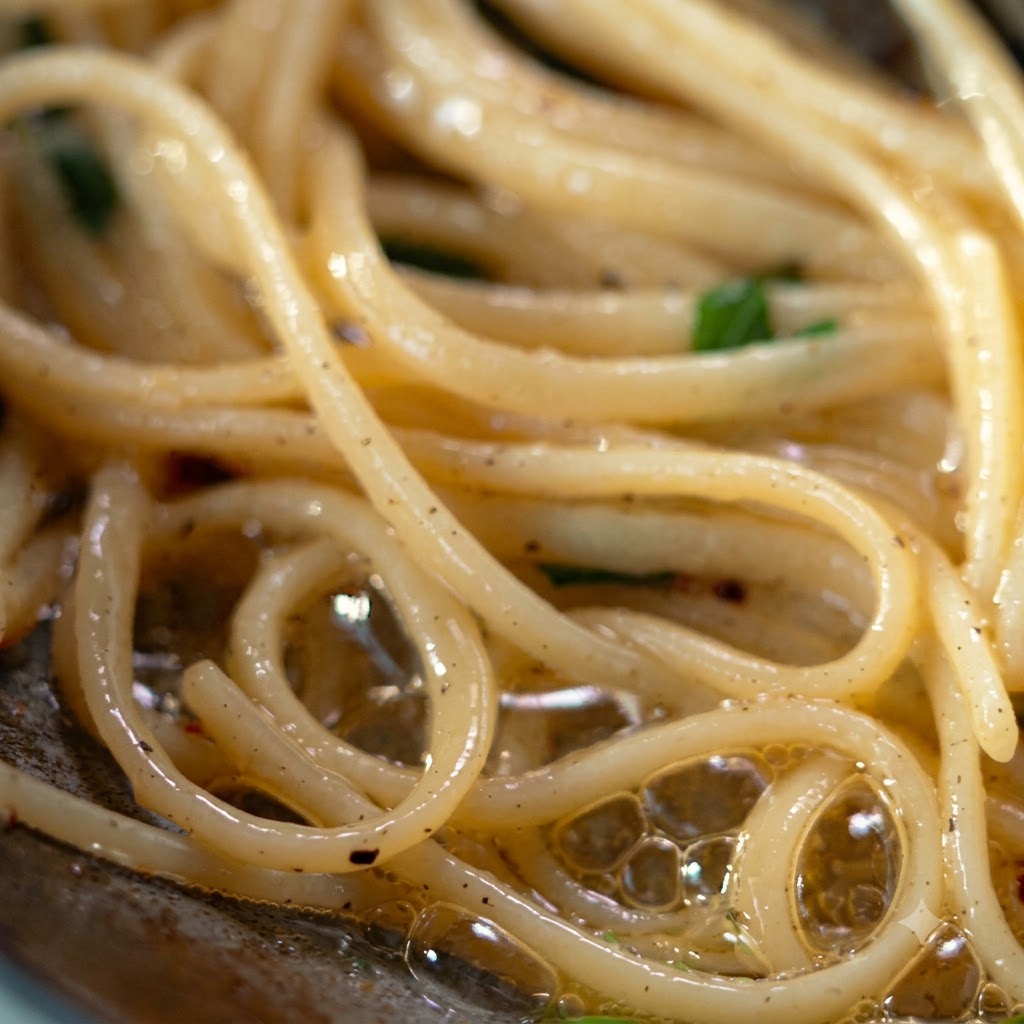 レードルとトングを使い、味付けされたパスタを持ち上げてシルバーの皿にきれいに移している様子。