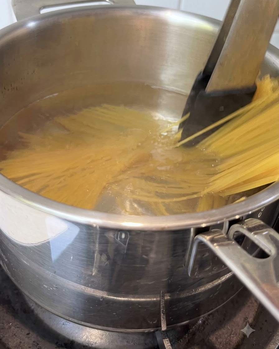 沸騰したお湯の入った鍋の中で、トングを使ってスパゲッティが混ぜられている様子。