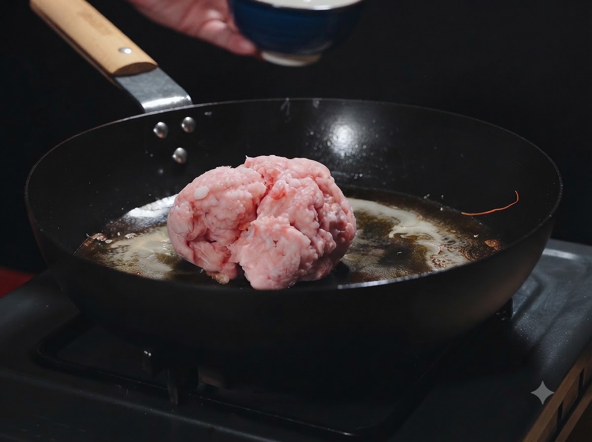 エビ油が残る熱いフライパンに、生のひき肉の塊を加えようとしている様子。