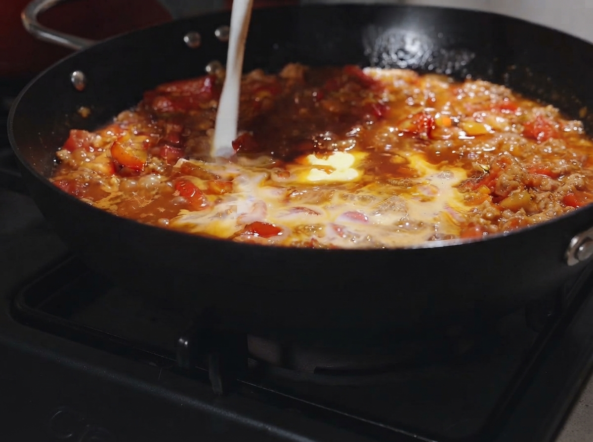 煮立っているトマトミートソースに、バターひとかけらと牛乳を注ぎ入れている様子。