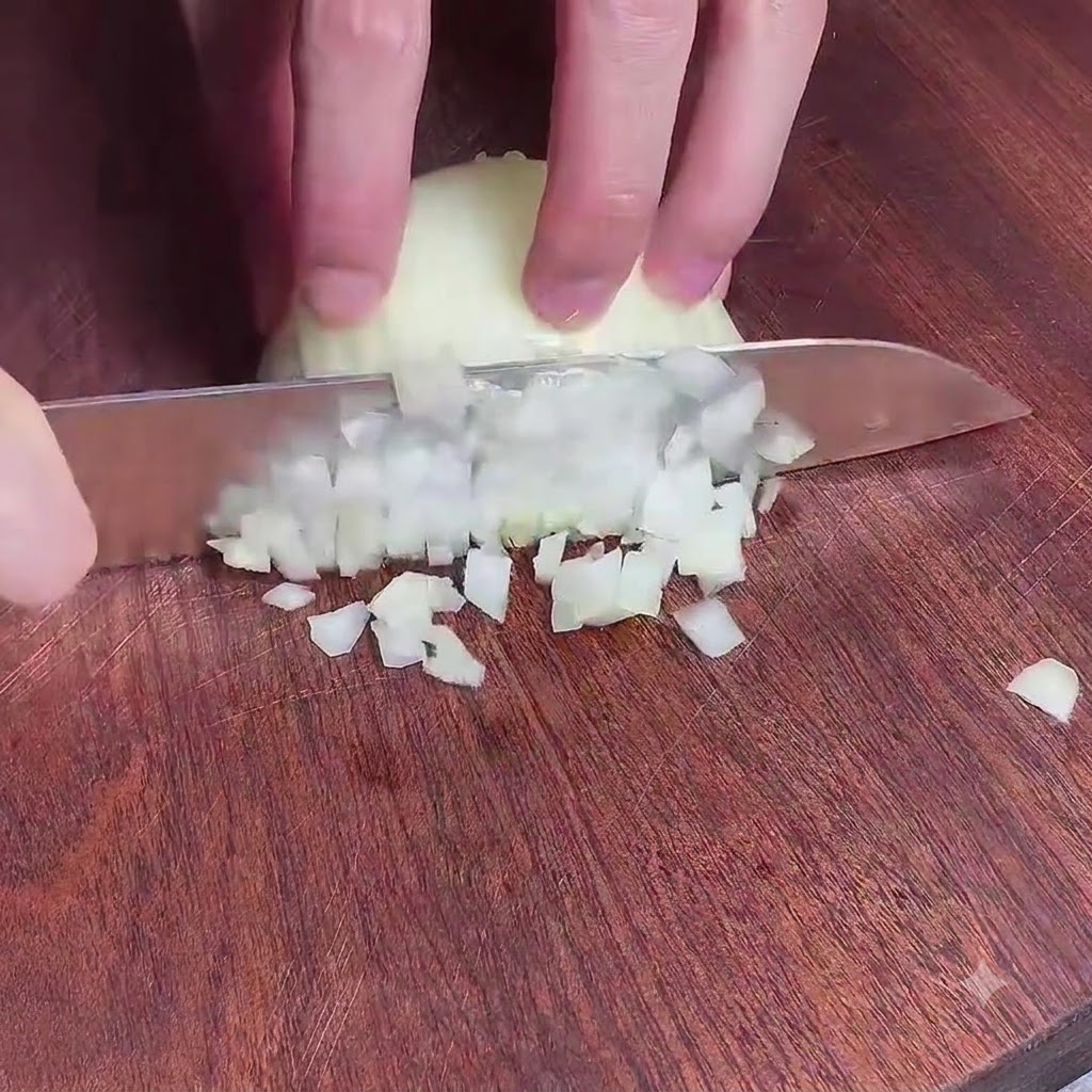 木製のまな板の上で包丁を使って玉ねぎを細かくみじん切りにする様子