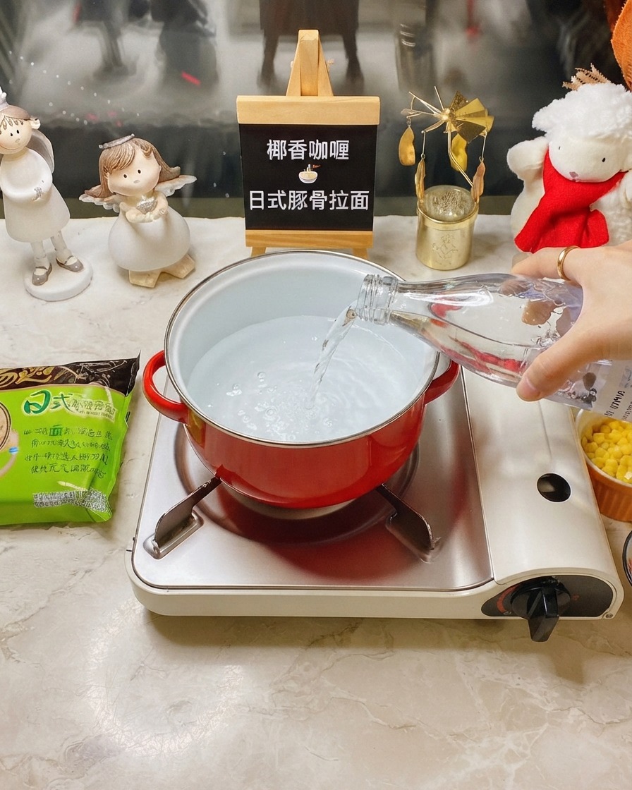携帯用コンロに置かれた赤い小鍋に、透明なボトルから水が注がれている様子。