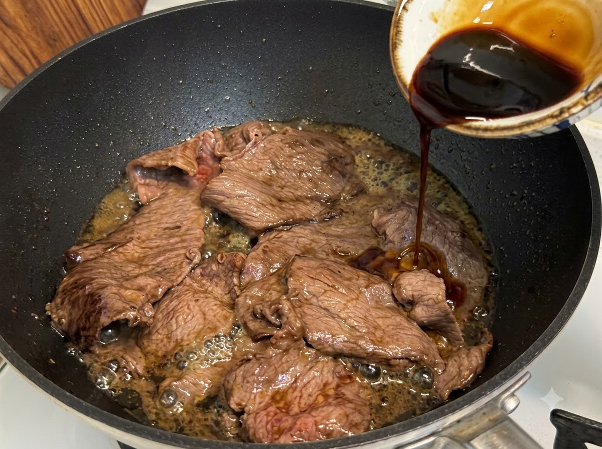 炒めた牛肉の入ったフライパンにテリヤキソースを回し入れ、煮詰めている様子。
