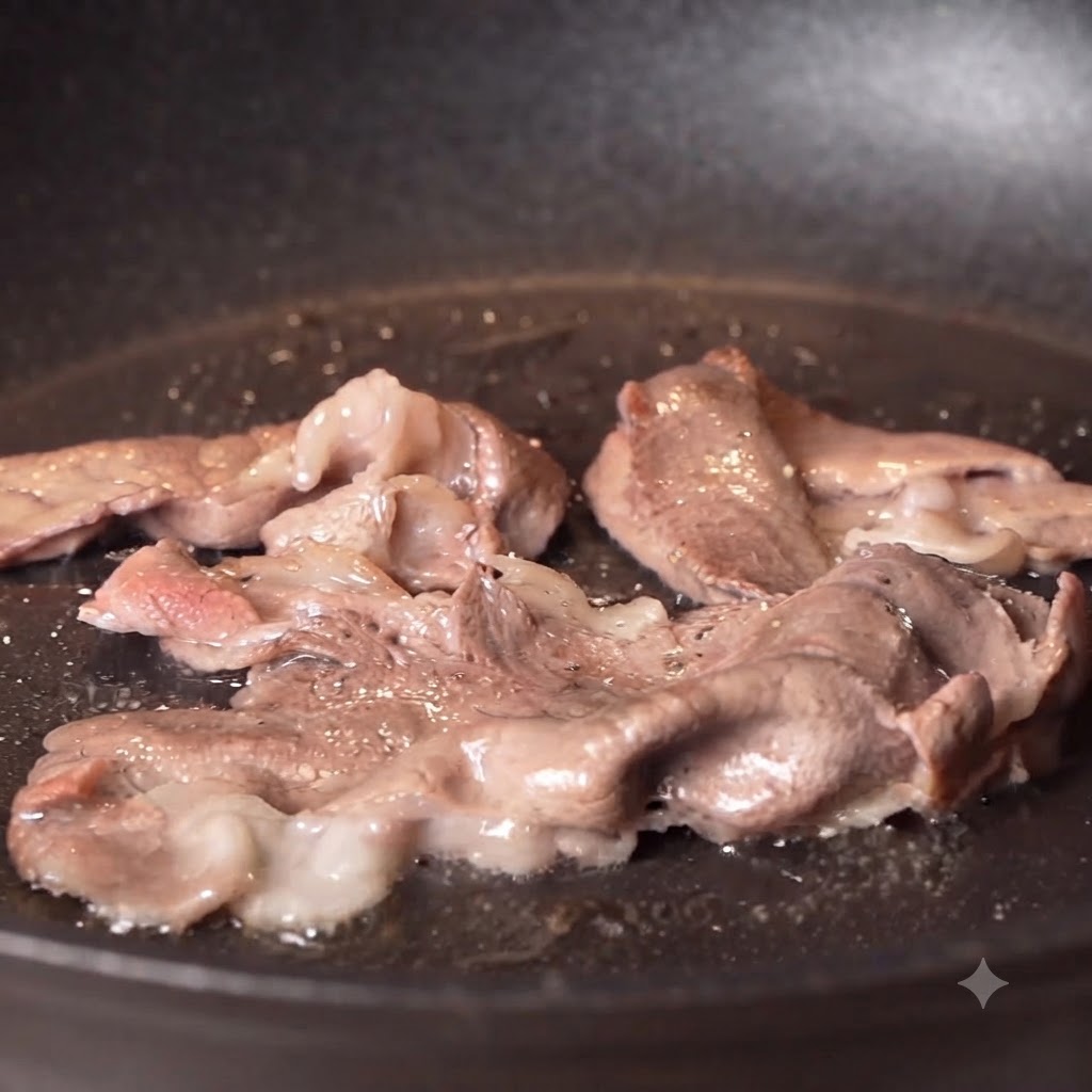 フライパンで調理中の焼き色がついた牛肉に、黒こしょうと塩を振りかけている様子