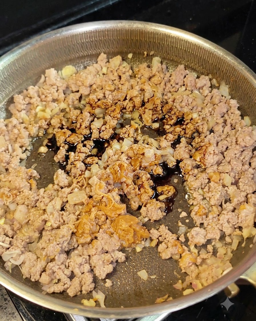 スプーンからフライパンのひき肉と玉ねぎに醤油が注がれている様子