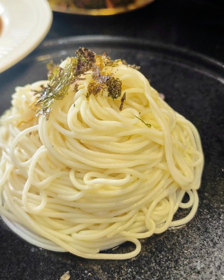 黒いお皿にきれいに盛り付けられたラーメンの上に砕いた乾燥海苔を振りかけている様子