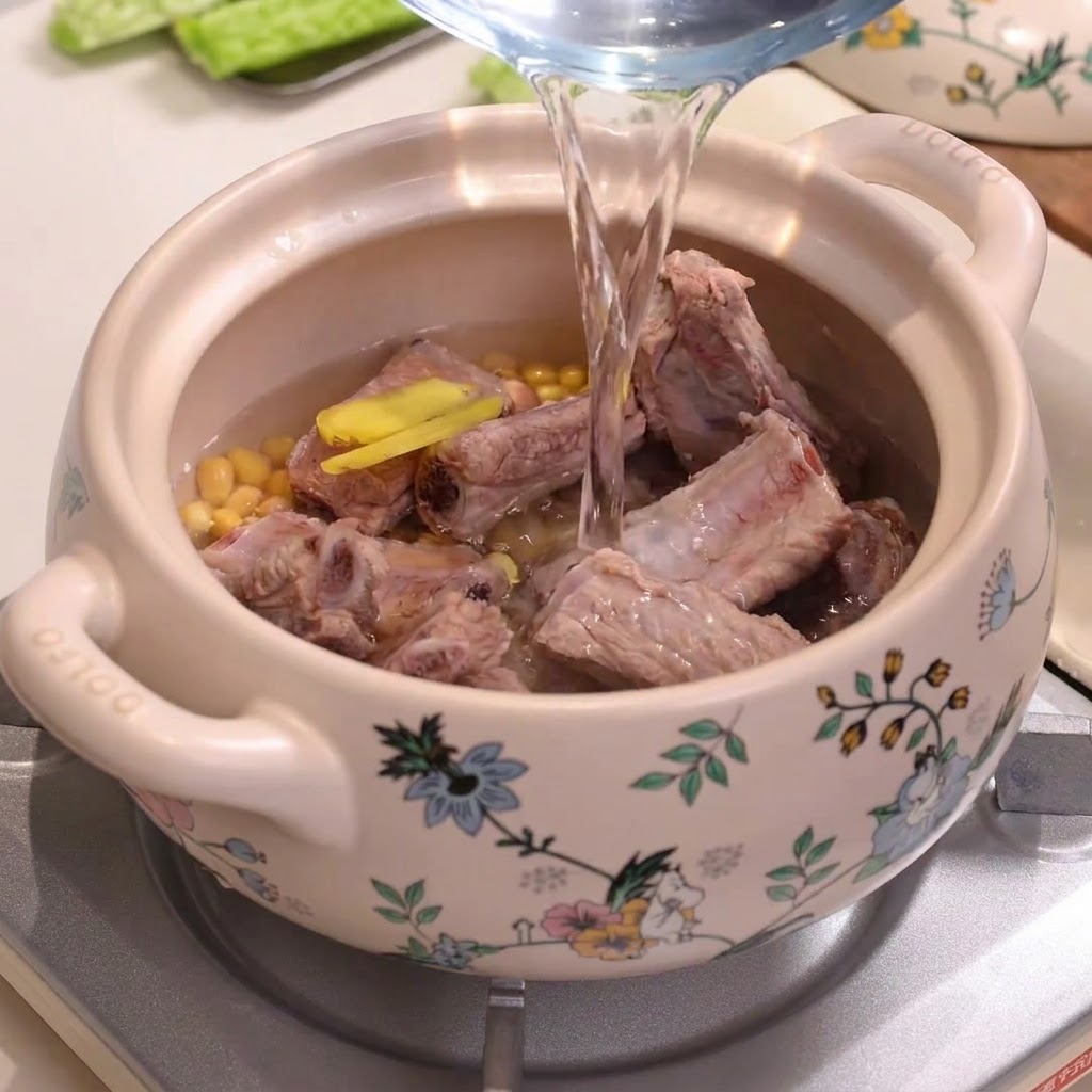 水正从玻璃量水壶倒入装满排骨和黄豆的装饰性陶瓷炖锅中。