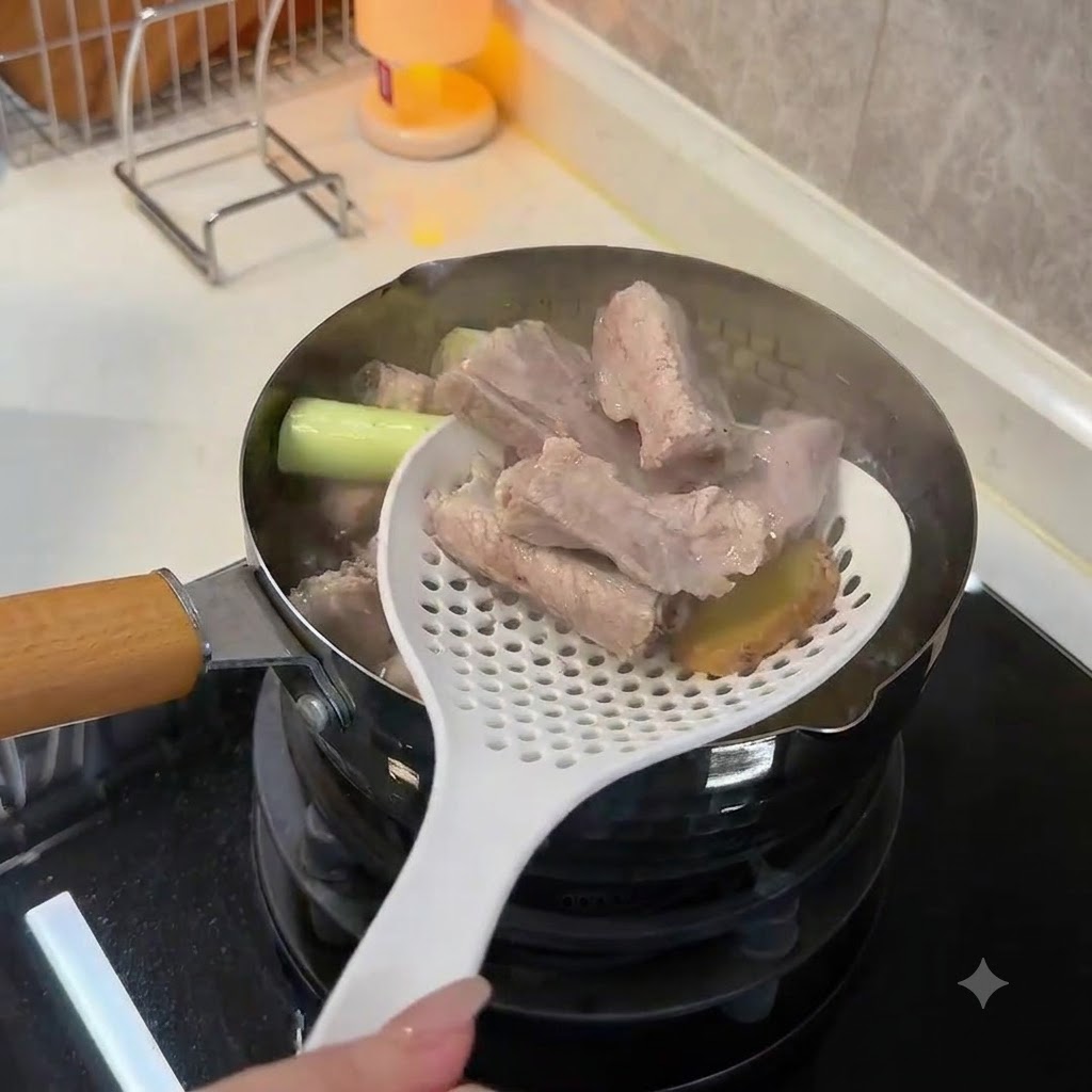 白い穴あきお玉を使って、沸騰したお湯から下茹でされた白濁した豚スペアリブと生姜のスライスを持ち上げているところ。