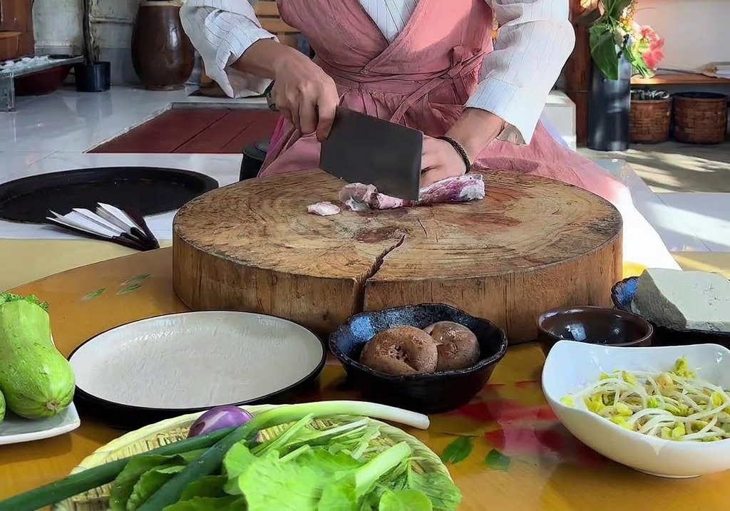 大きくて丸い木製のまな板の上で、包丁を使って生肉の豚バラ肉をスライスしている手。