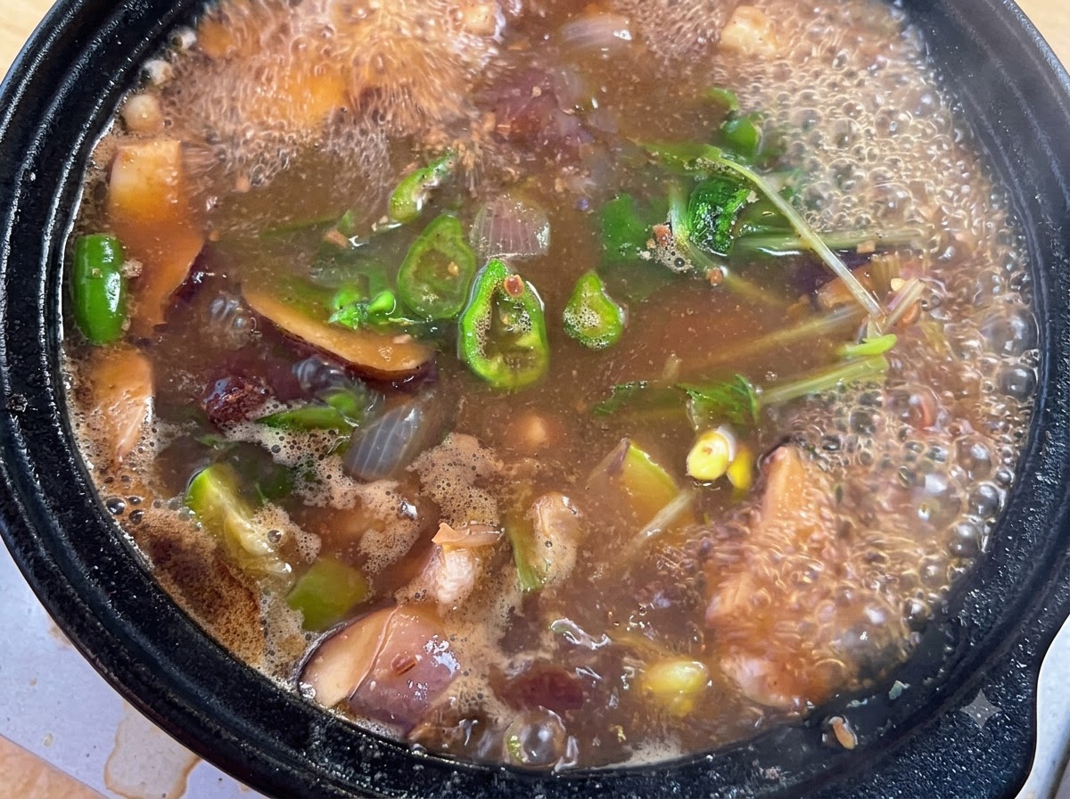 グツグツ煮立つスープの鍋に、牛肉ダシダ、粉唐辛子、刻みネギを加えている様子。