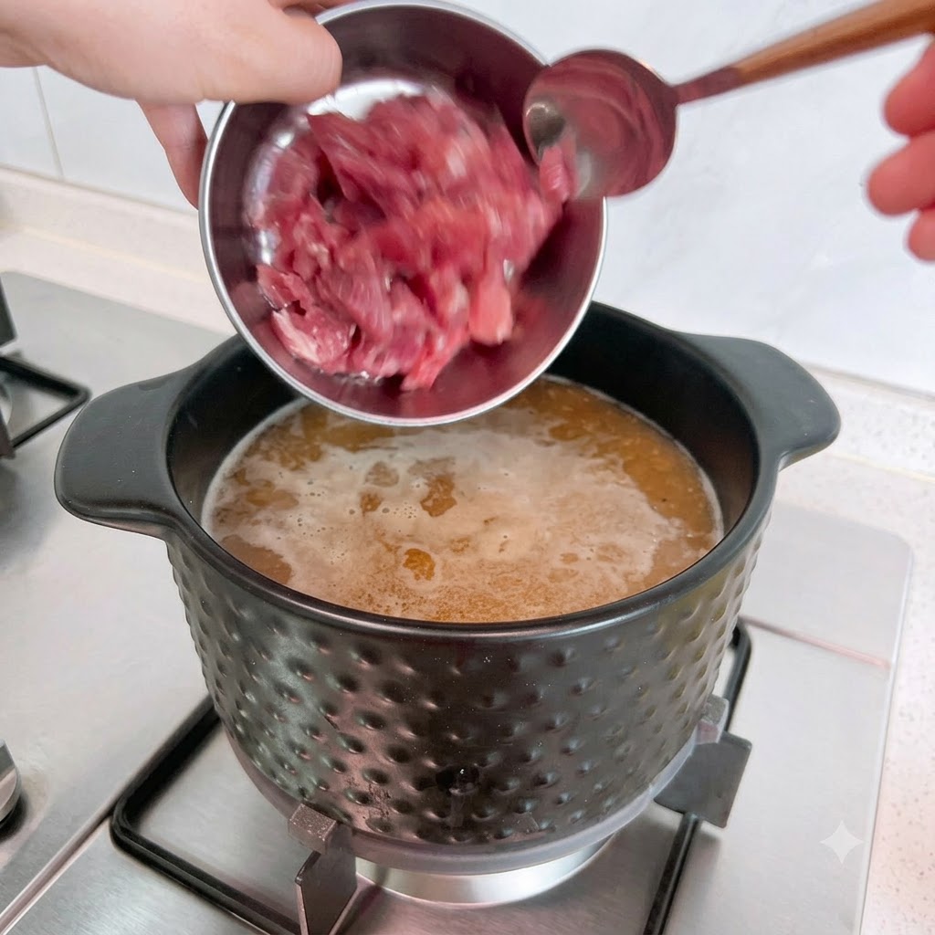 金属製のボウルから、沸騰したスープの入った鍋に生の豚肉を入れている様子。