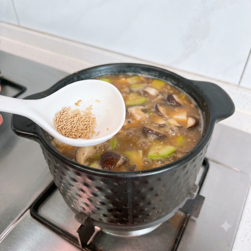 牛肉だしの素がのった白いスプーンを、ぐつぐつ煮えるテンジャンチゲの鍋の上で構えている様子。