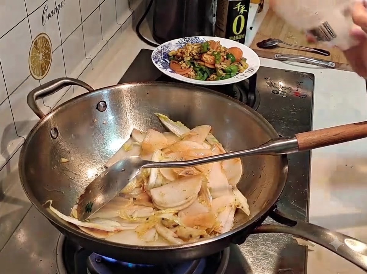 スライス野菜の入った中華鍋に向けて、袋から塩をパラパラと振りかけているところ。
