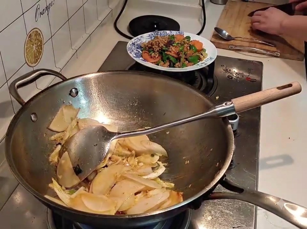 黒いケトルから、スライスした大根と白菜の入った中華鍋に水が注がれているところ。