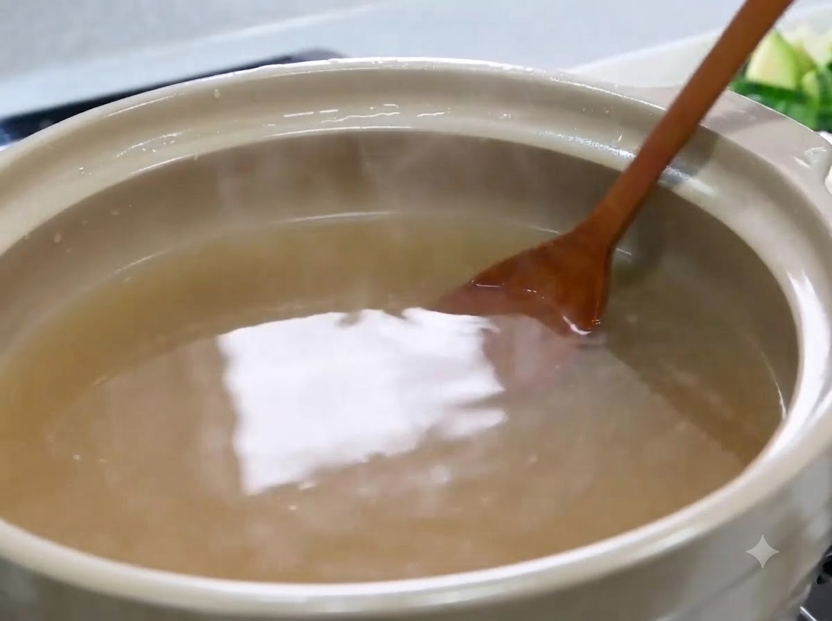 薄茶色のスープが入った鍋の中で、木べらが味噌をかき混ぜて溶かしている様子。