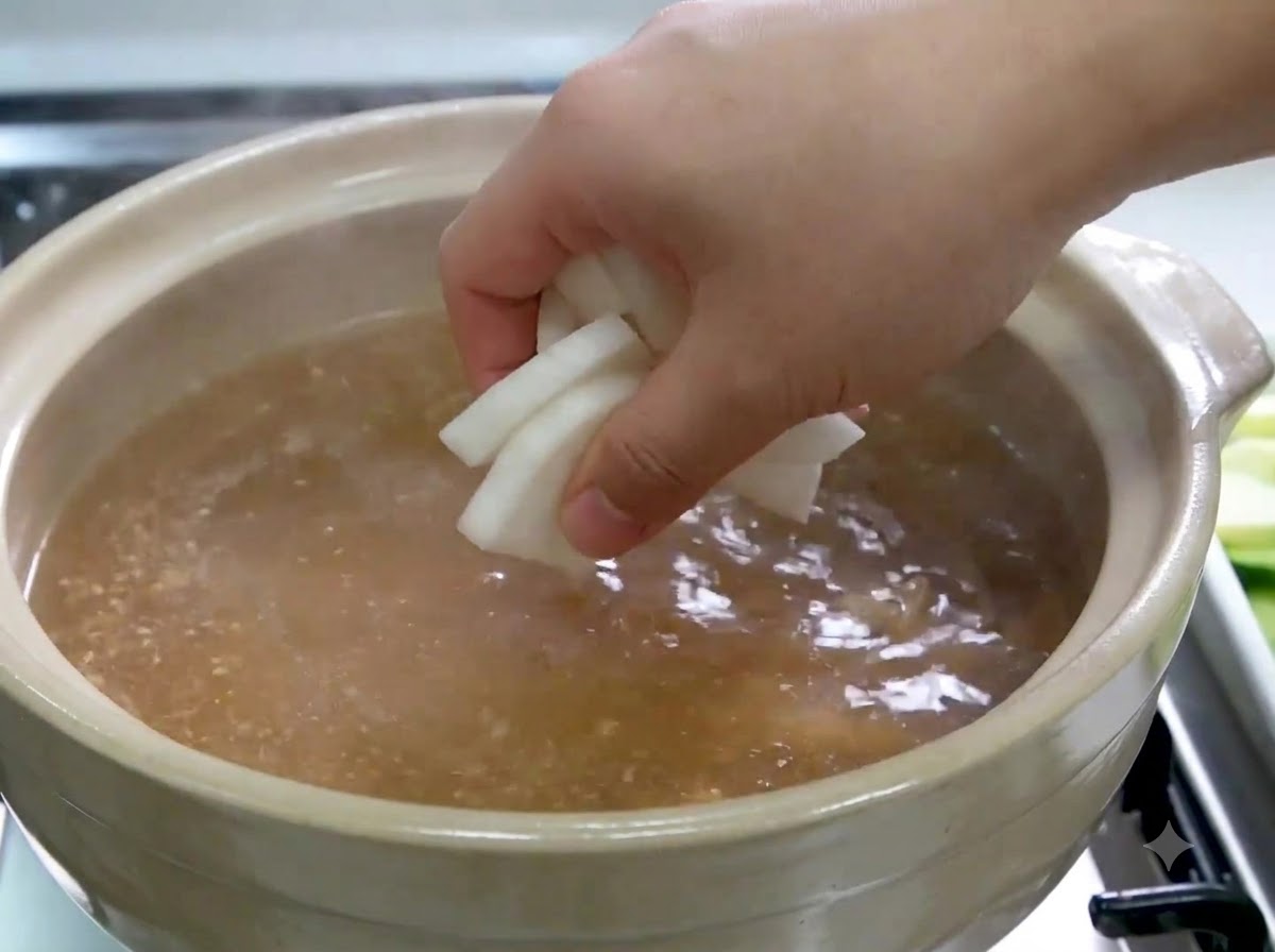 煮立っているスープの中に、手で大根のスライスを入れている様子。