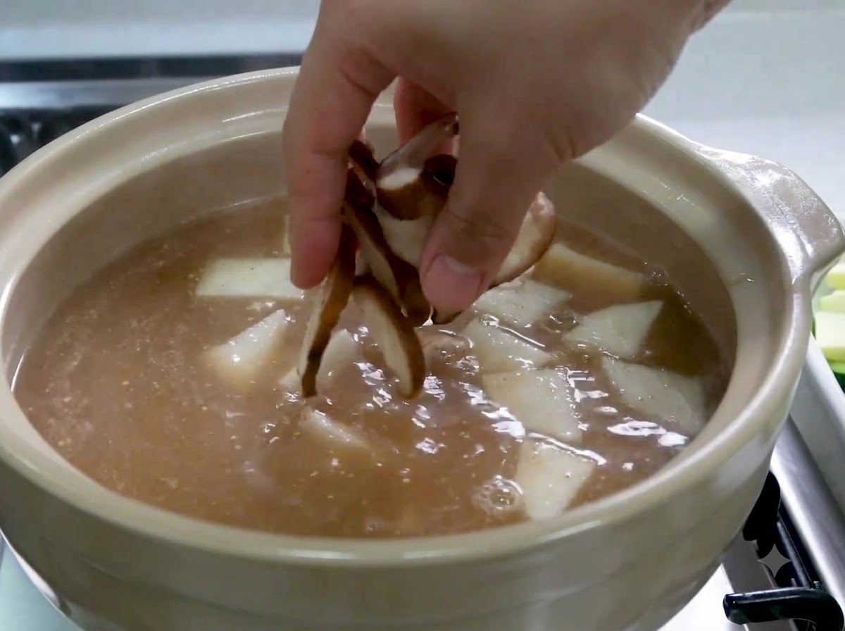 スープと大根が入った鍋に、スライスした椎茸を手で入れている様子。