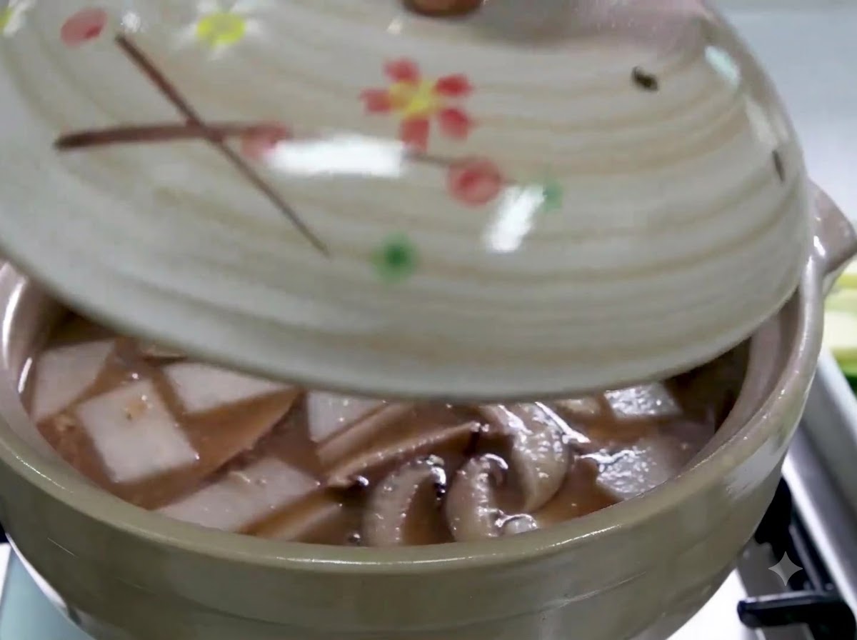 スープ、スライスした大根、椎茸が入った土鍋に蓋をしている様子。