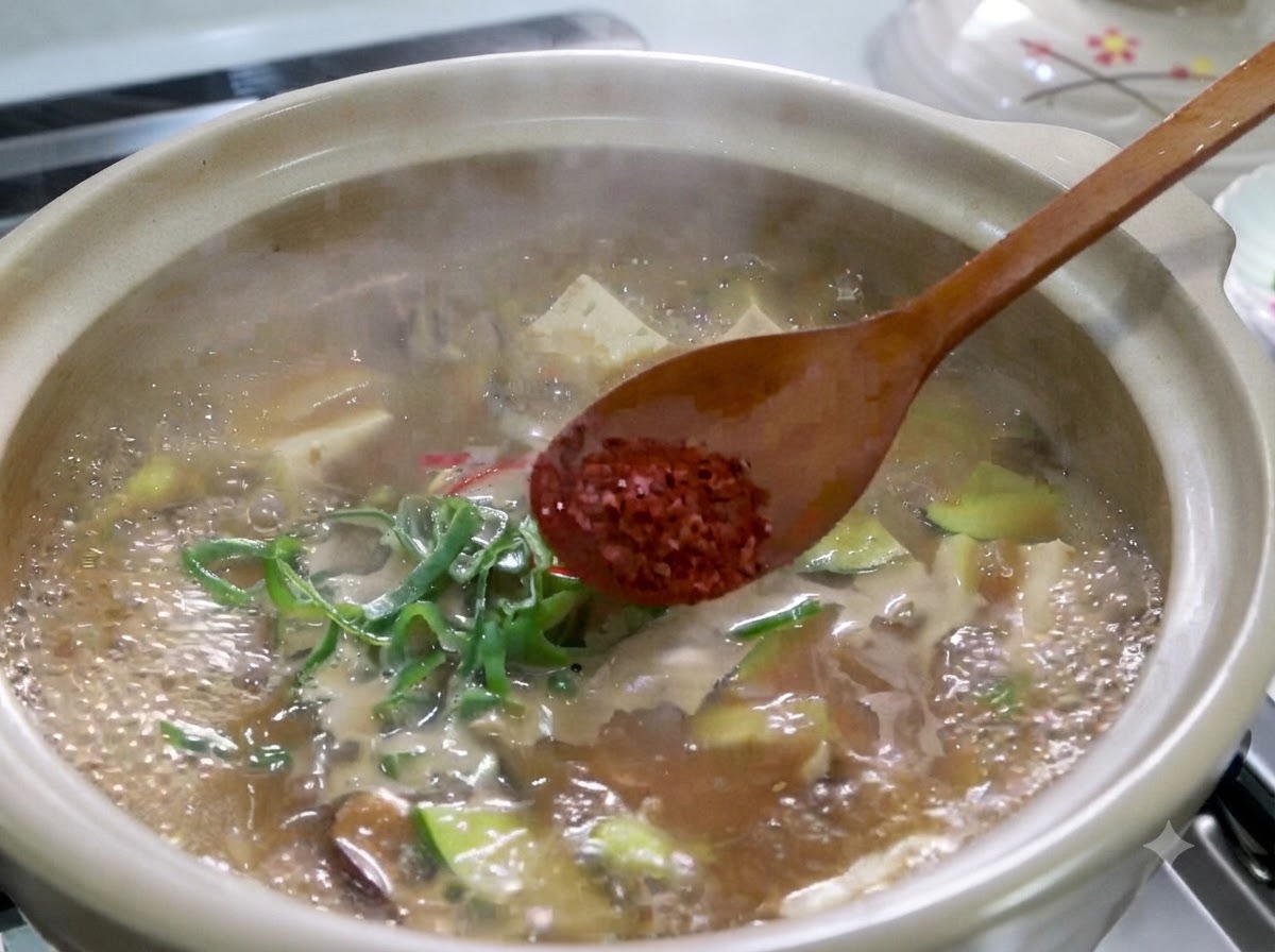 韓国の味噌チゲの沸騰した鍋の上で、赤い粉唐辛子を乗せた木べらがある様子。