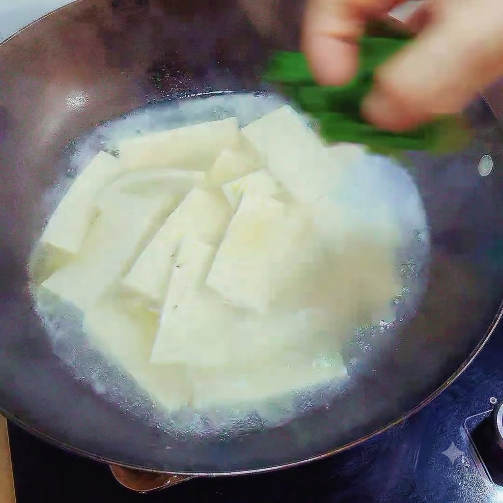 完成した豆腐スープの上に、刻んだ緑のネギを上から落としている様子。