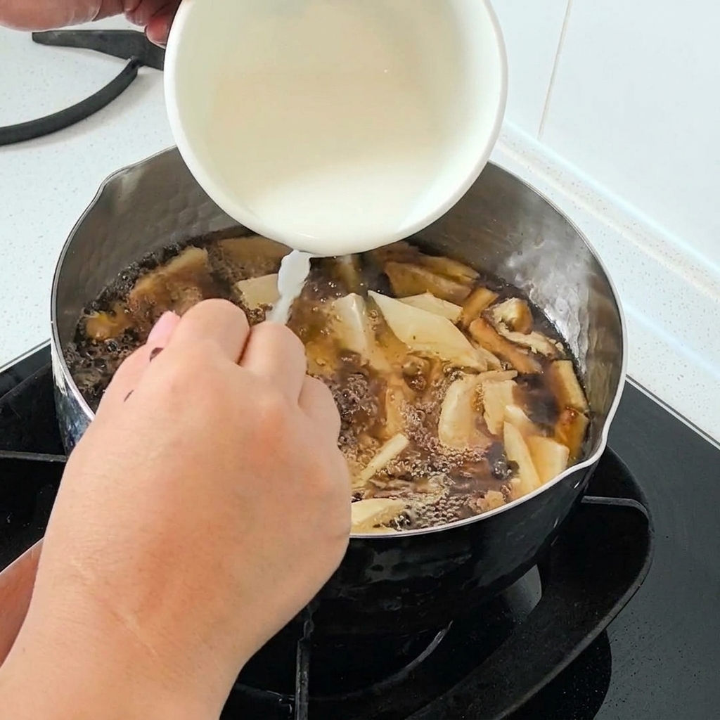 グツグツと煮立つスープの入った鍋に、白いボウルから水溶きくわい粉を注いでいる様子。