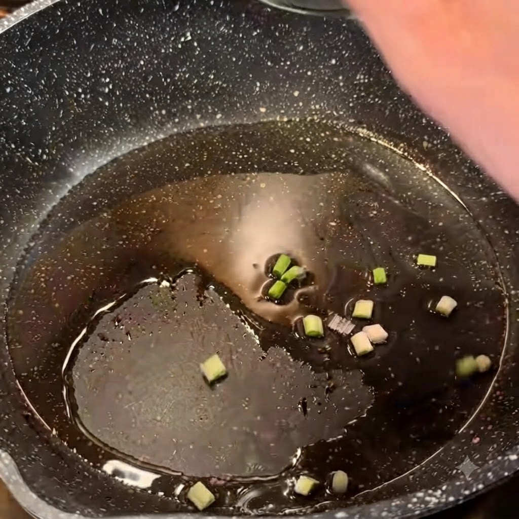 黒いまだら模様のフライパンの中で、熱した油で刻んだ青ねぎがジュージューと炒められている様子。