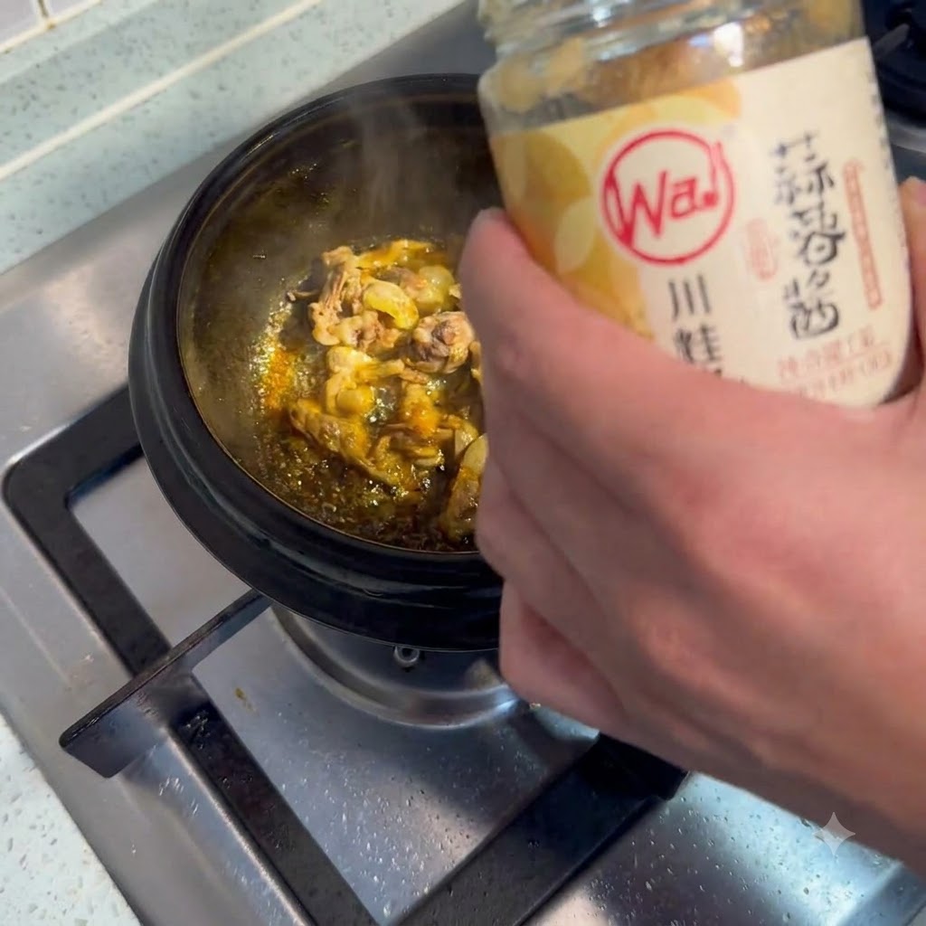 スプーンですくったにんにくペーストを、お肉を炒めている鍋に加えている様子。