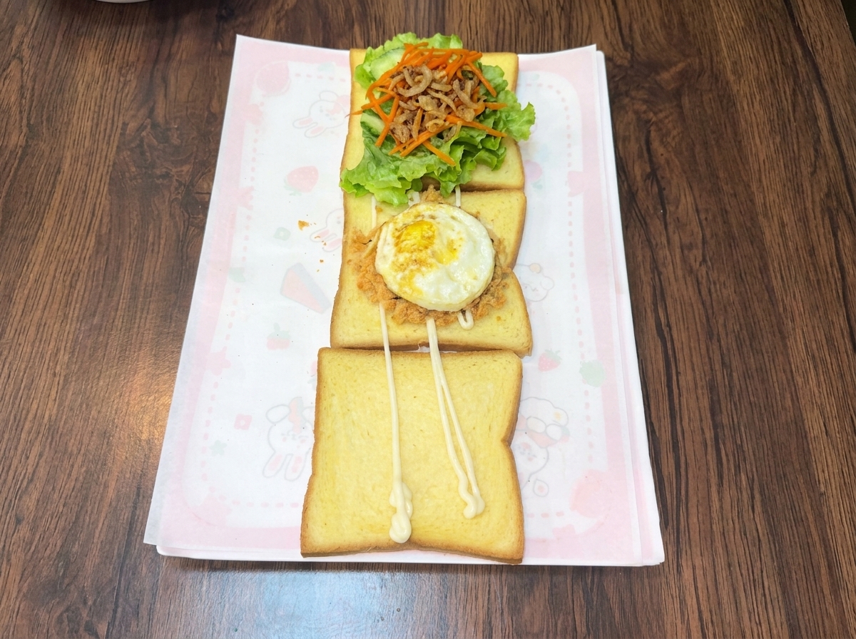 肉でんぶと海苔を乗せたトーストの上に、焼きたての目玉焼きを置いている様子。