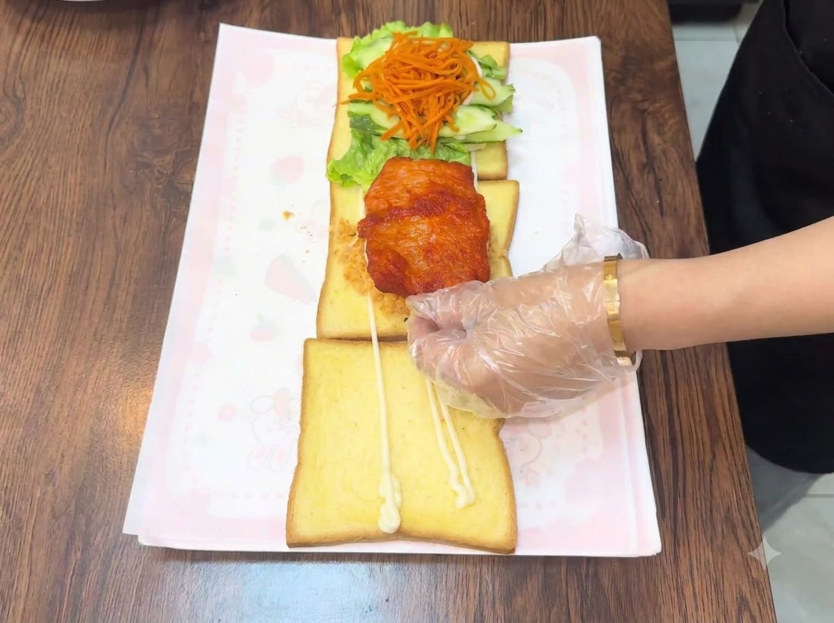 温かいフライドチキンカツを、重ねたトーストの上に乗せている様子。