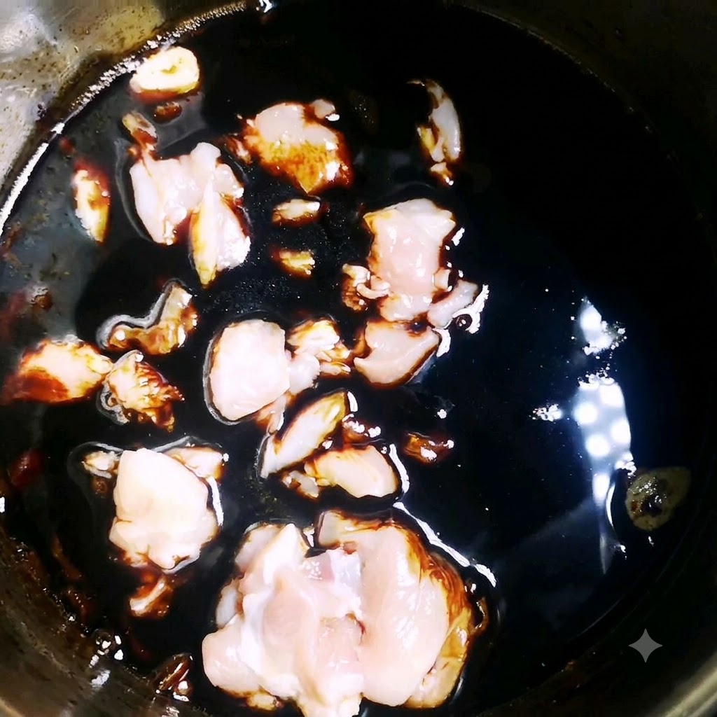 鍋の中の濃い風味のソースの中で、生の鶏肉のピースが煮込まれている様子。