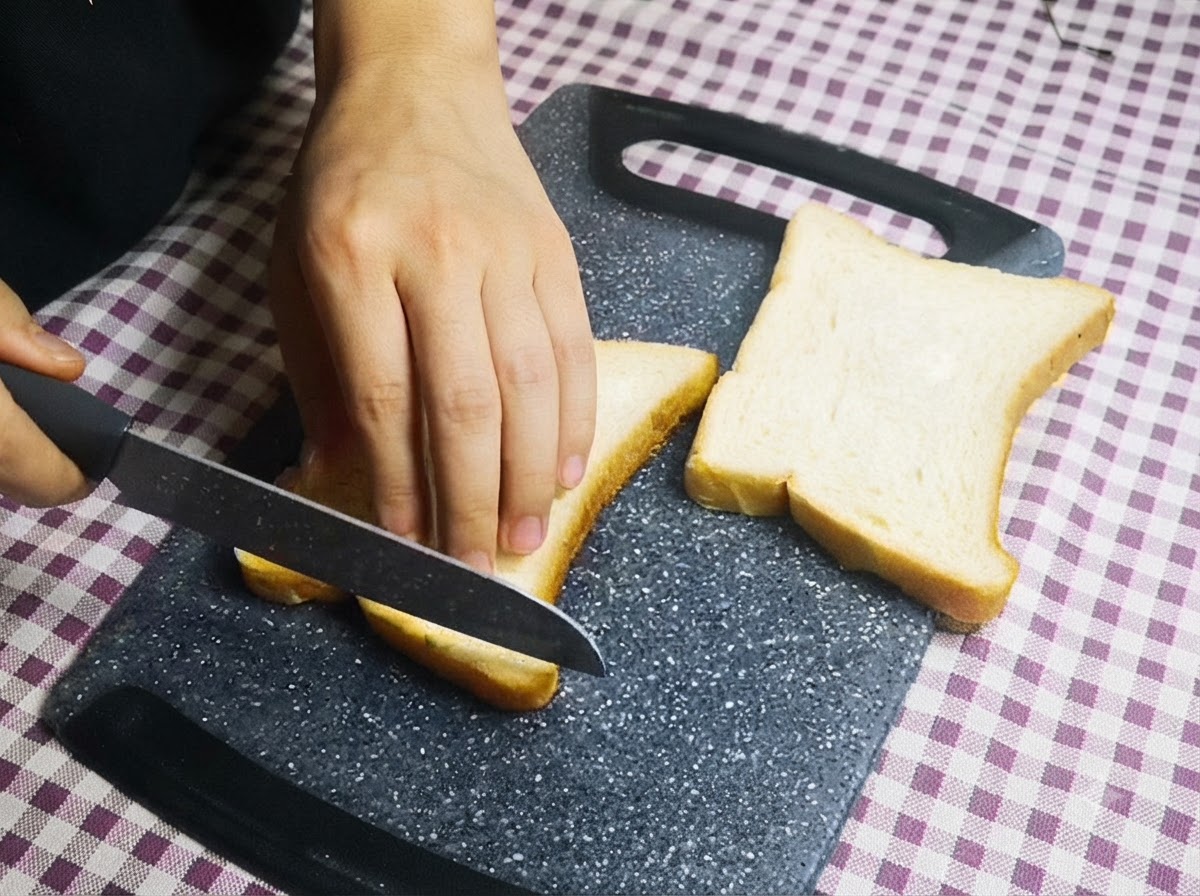 まな板の上でナイフを使い、食パンの4面の耳を切り落としている様子。