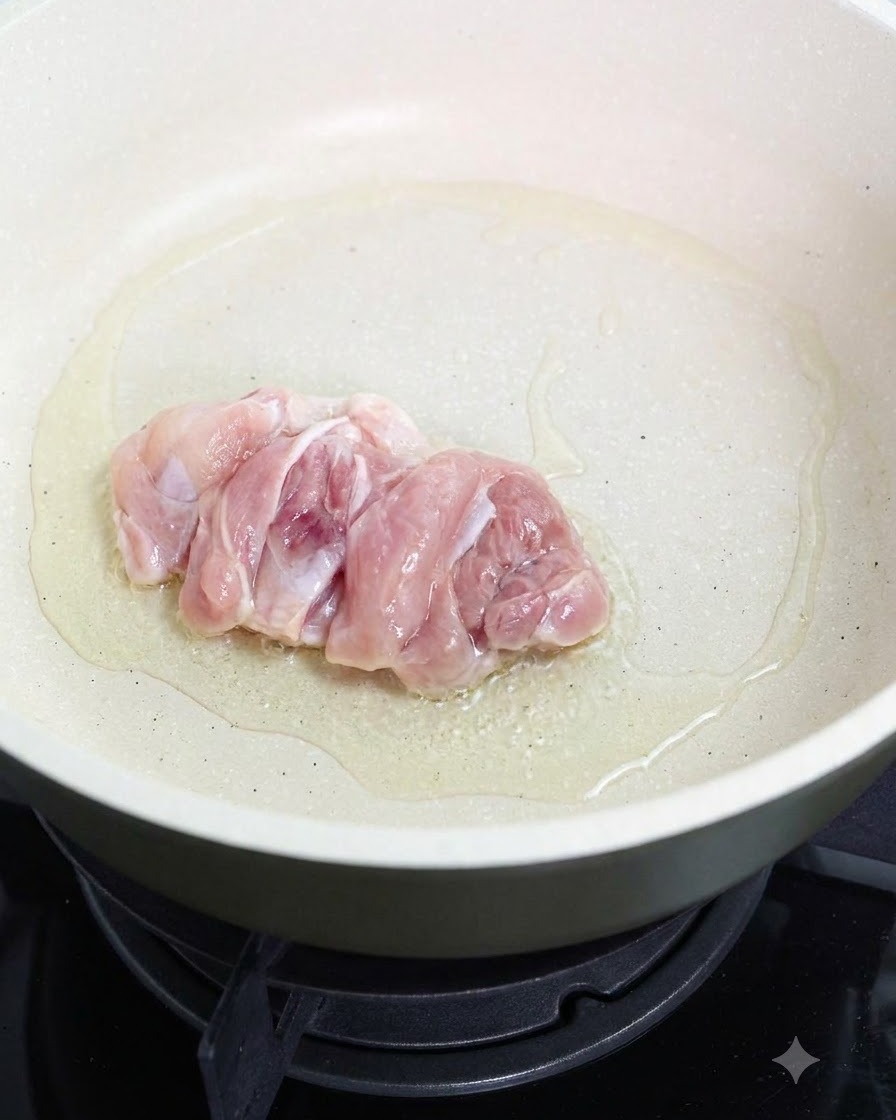 油をひいたフライパンで生の鶏もも肉を皮目から焼いている様子。